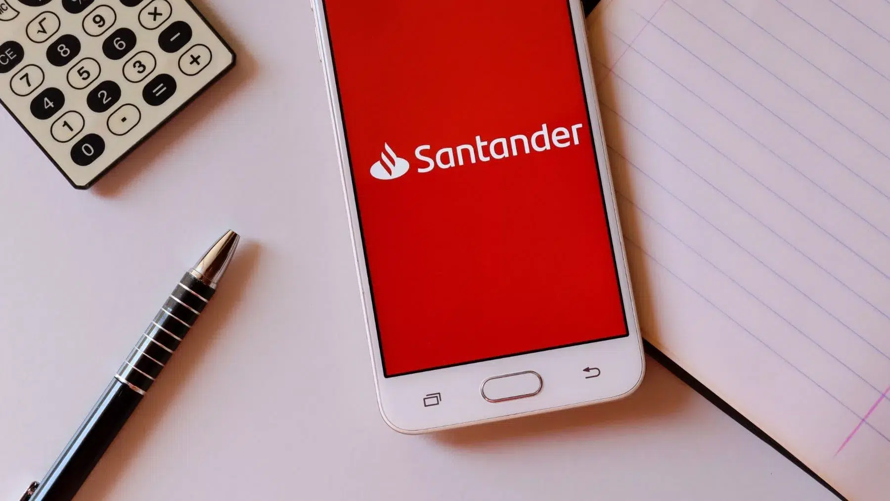 Teléfono móvil con el logo del Banco Santander junto a un bolígrafo y una calculadora