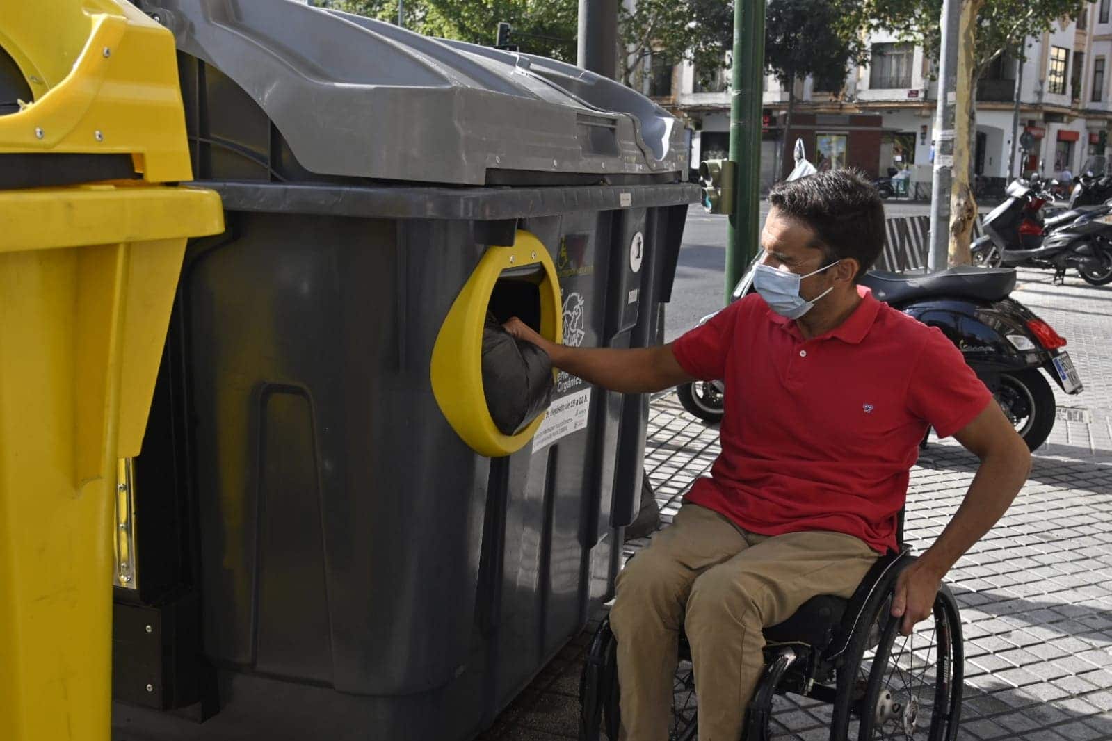 Usuario silla de ruedas arrojando bolsa de basura en contenedor accesible