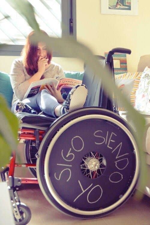 Una chica sentada en el sofá y sus pies en una silla de ruedas donde pone "sigo siendo yo"