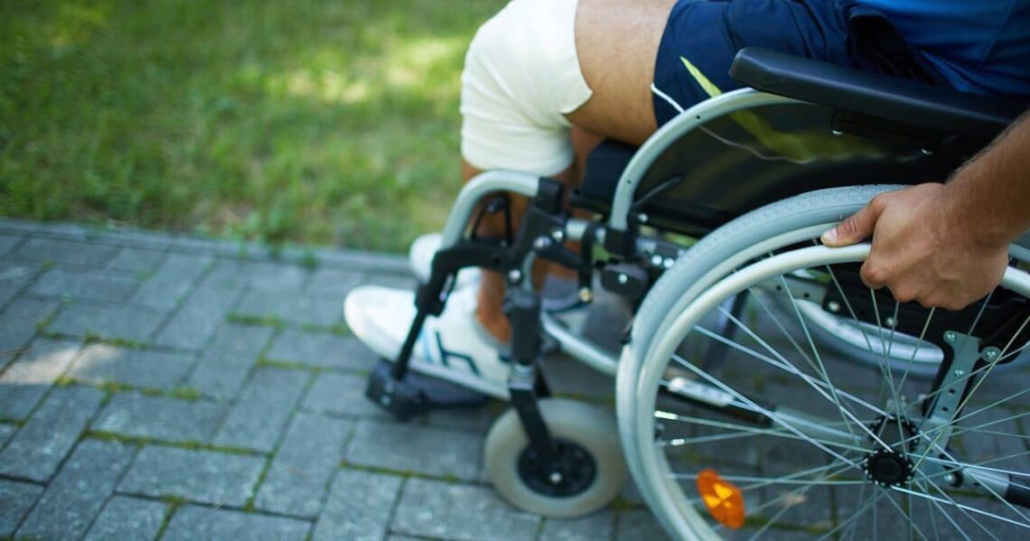 Mano en el aro de la silla de ruedas. Se ve parte del suelo