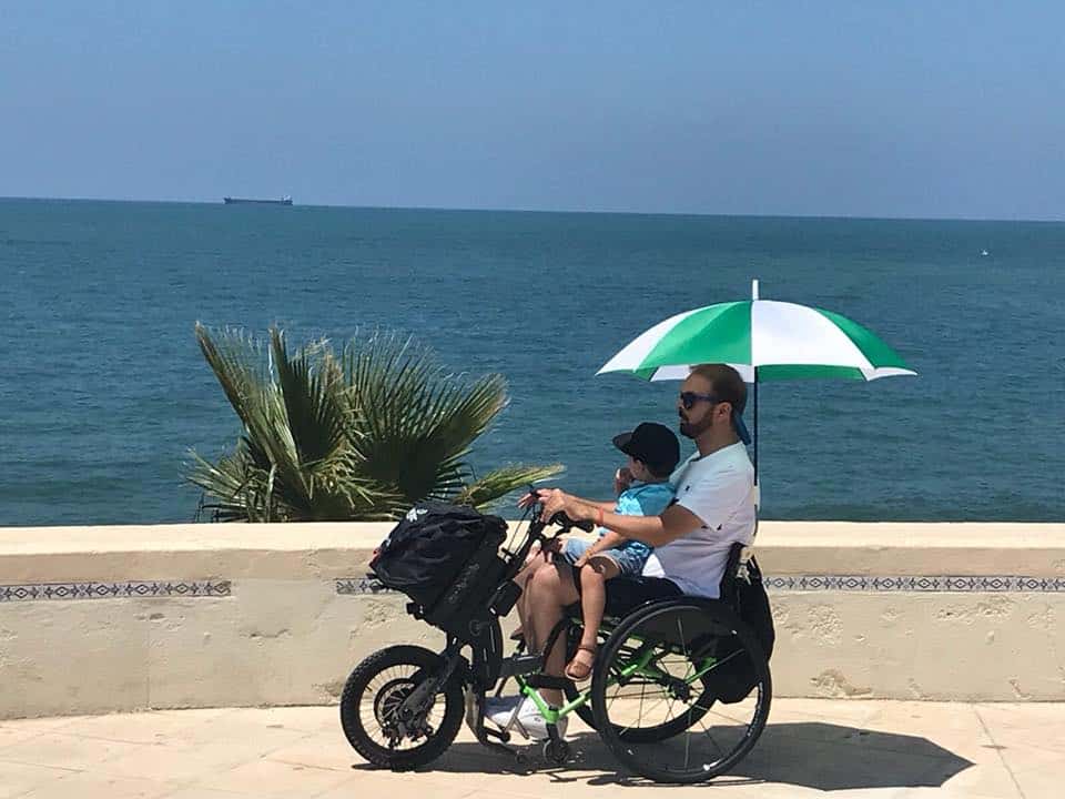 Usuario de silla de ruedas con su Batec e hijo encima
