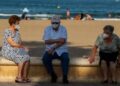 Turismo Imserso: Tres personas mayores descansan en el paseo marítimo de la playa de la Malvarrosa