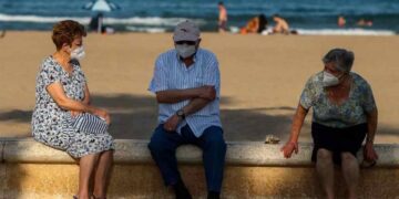 Turismo Imserso: Tres personas mayores descansan en el paseo marítimo de la playa de la Malvarrosa