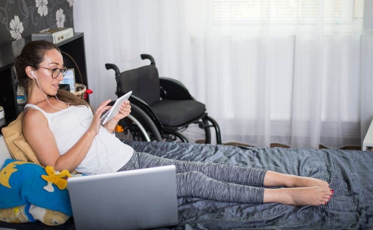 Persona con discapacidad tumbada en su cama y navegando por Internet