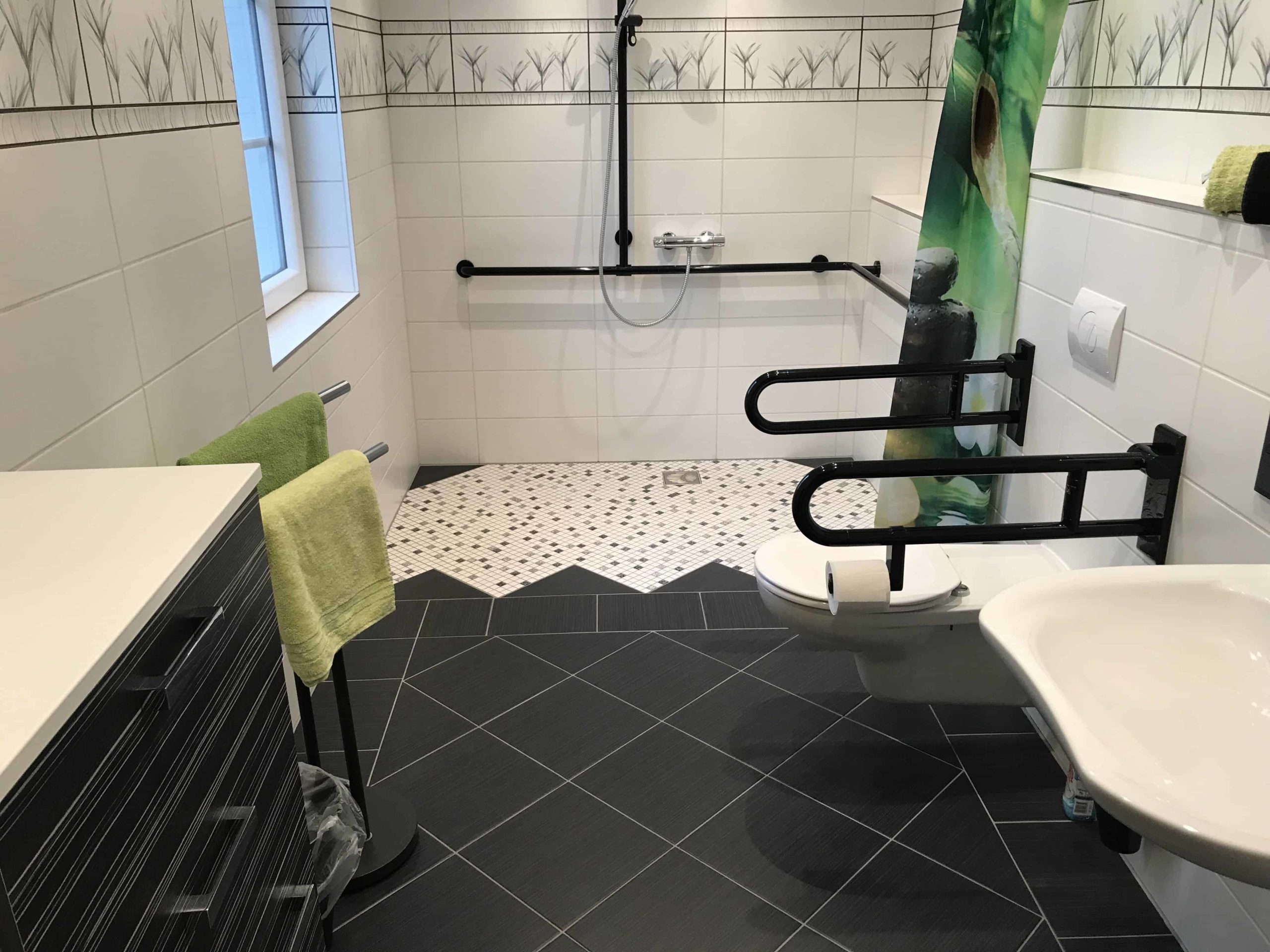 Baño accesible de tonos negro, blanco y verdes. Placa ducha y water con asideros
