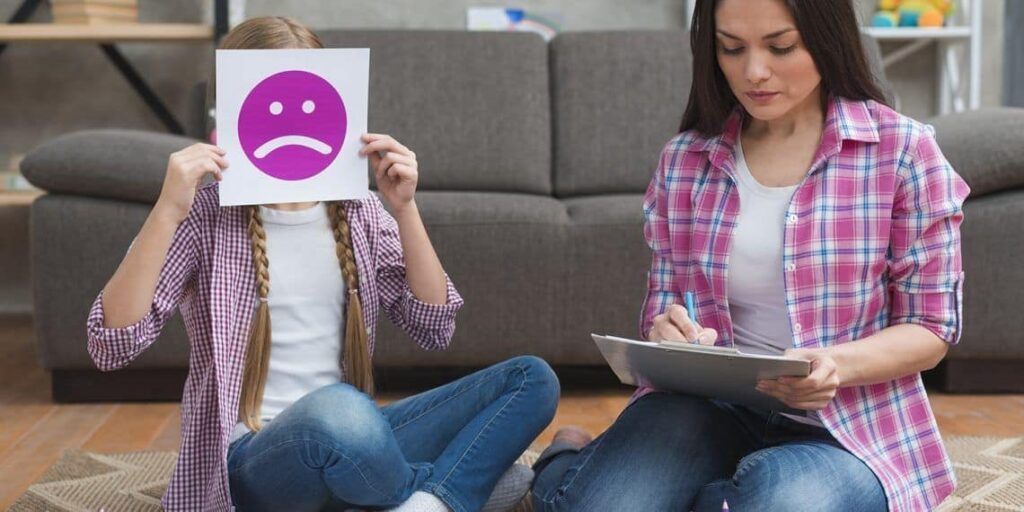 Niña junto a su madre con un cartel de una carita triste