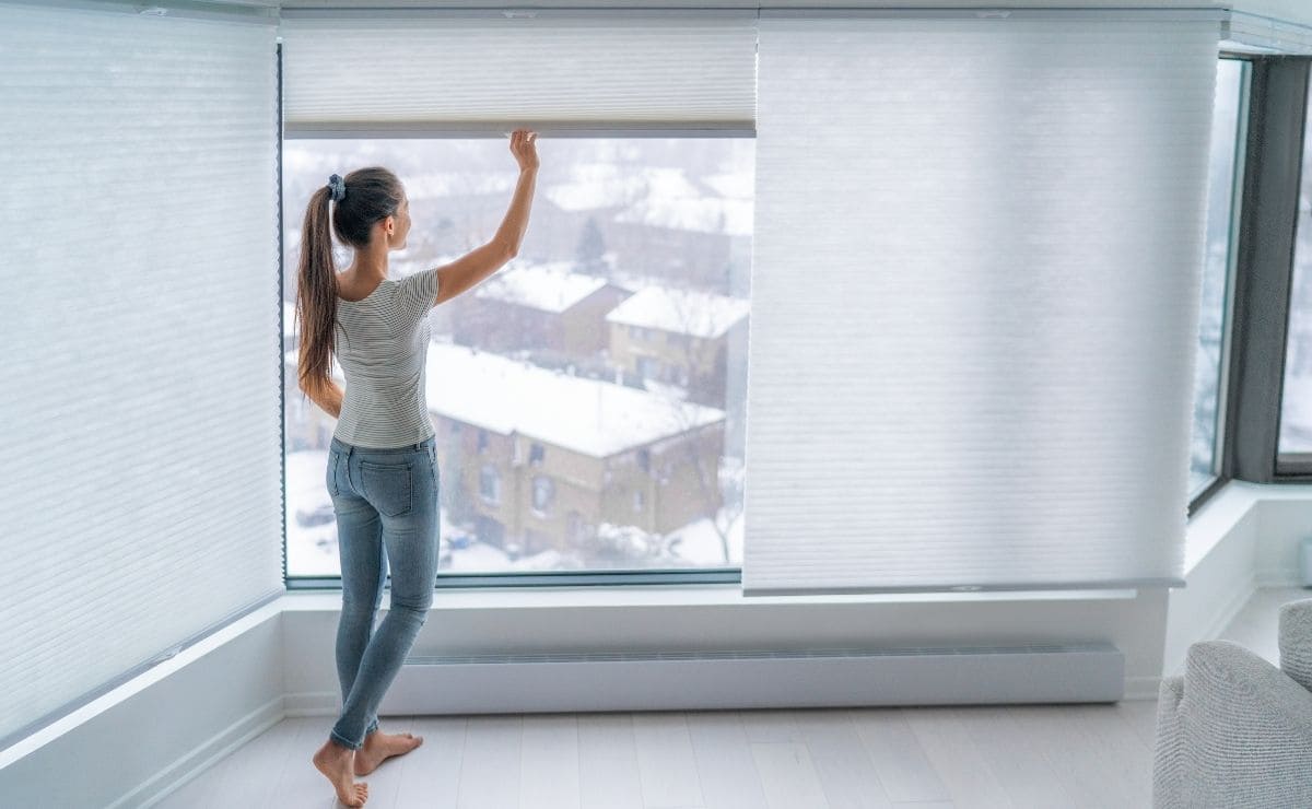 Mujer cerrado cortinas para conservar la temperatura del aire acondicionado