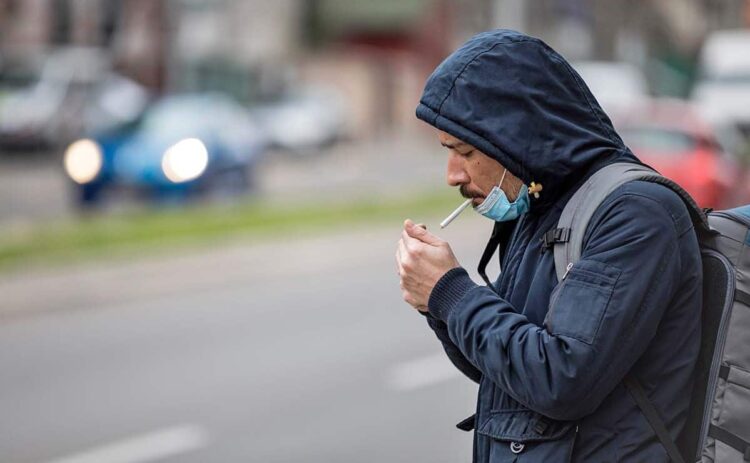 Persona fumando un cigarro con mascarilla