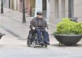 Anciano con discapacidad junto a su silla de ruedas por la calle