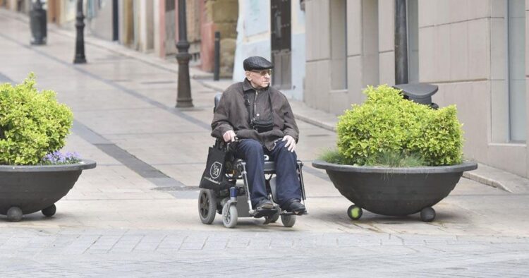 Anciano con discapacidad junto a su silla de ruedas por la calle