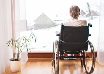 Mujer mayor en silla de ruedas mirando a la ventana. Soledad y dependencia