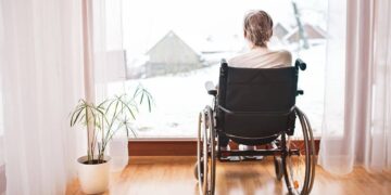 Mujer mayor en silla de ruedas mirando a la ventana. Soledad y dependencia