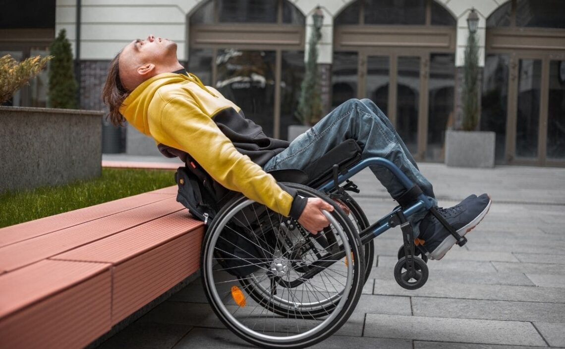 Persona en silla de ruedas se apoya el respaldad de su silla de ruedas ante un banco