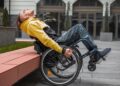 Persona en silla de ruedas se apoya el respaldad de su silla de ruedas ante un banco