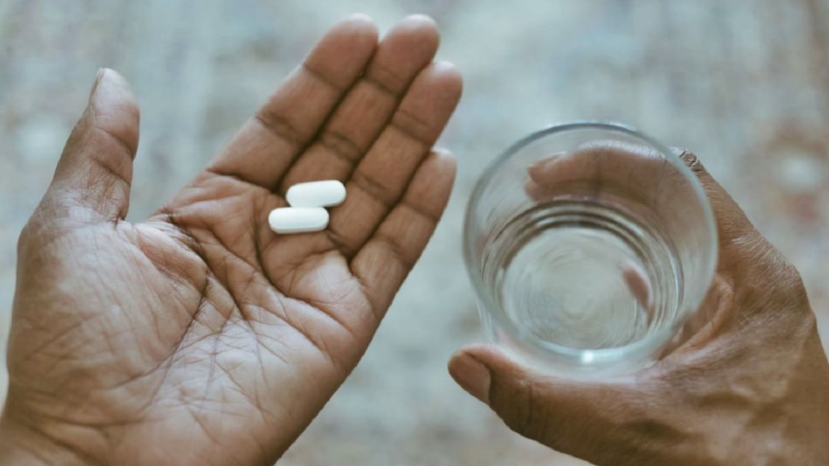 Mano con pastillas y vaso de agua