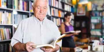 Persona mayor lee un libro en una biblioteca