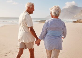 Pareja de personas mayores pasean por una playa durante un viaje del IMSERSO