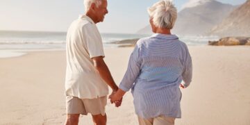 Pareja de personas mayores pasean por una playa durante un viaje del IMSERSO
