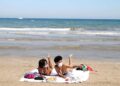 Mujeres toman el sol en la playa con mascarillas en verano